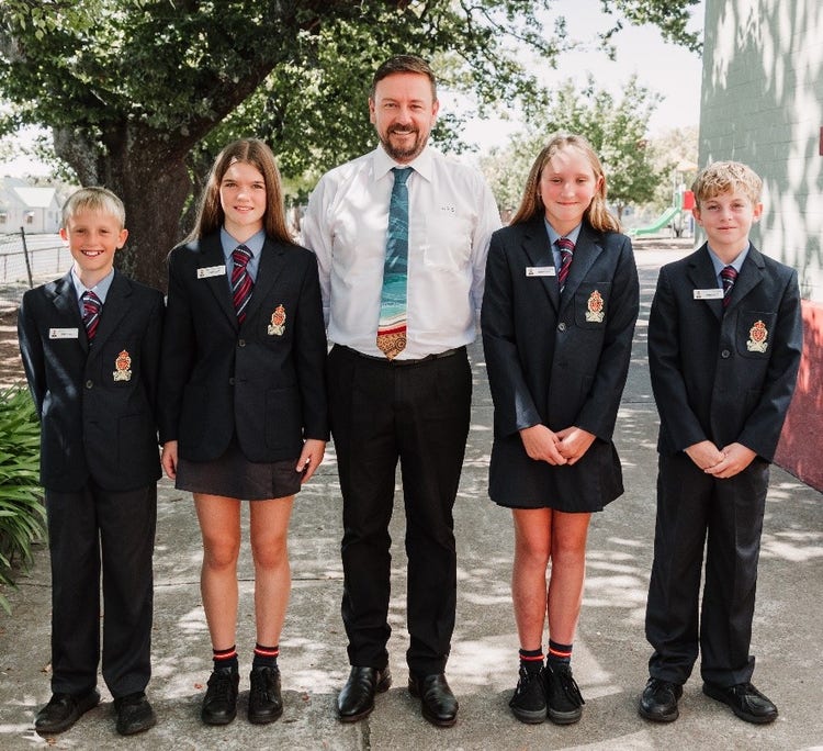 Principal with four student prefects outside smiling under the shade of a tree
