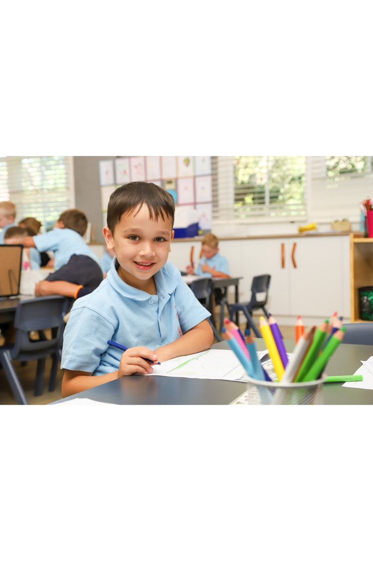 student sitting at desk colouring smiling at camera