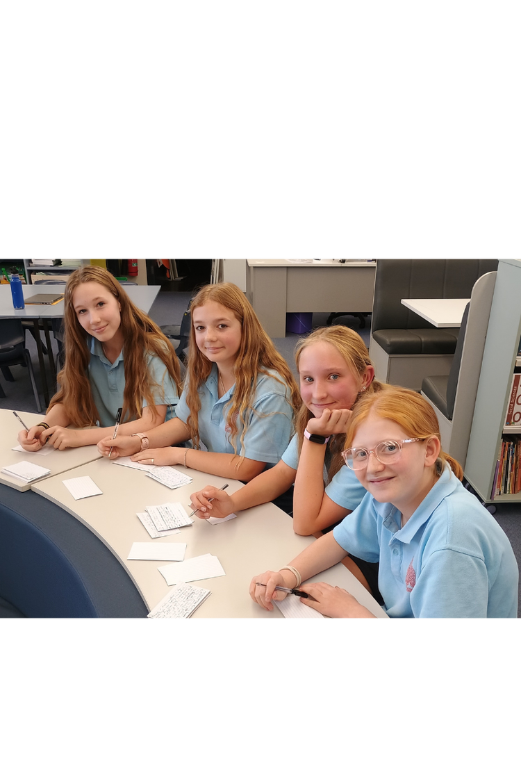 Four girls smiling at the camera whilst writing debating palm cards